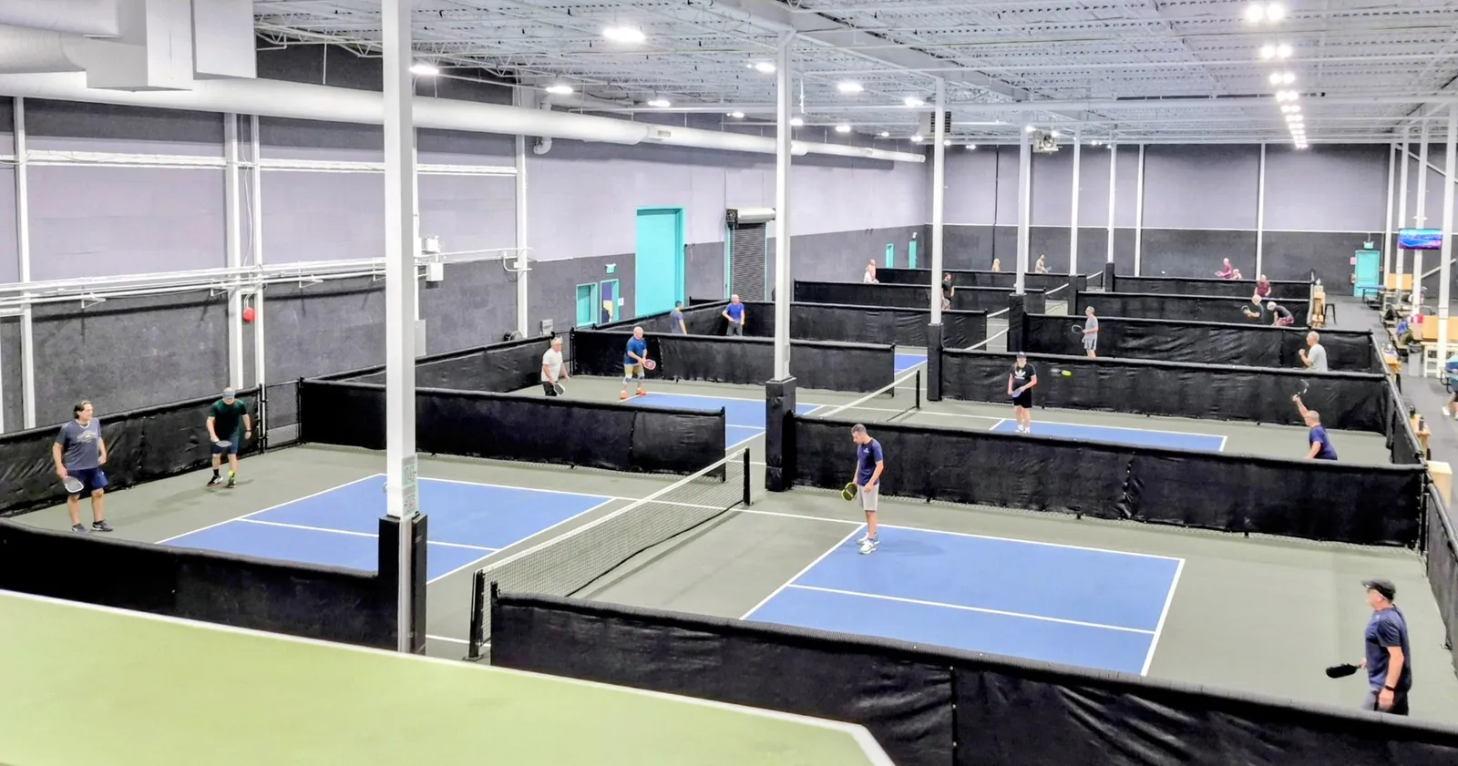 Indoor pickleball courts divided by chain link fence with black windscreen